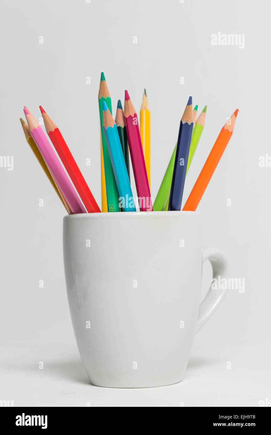 A group of multi colored pencils in a white cup on an isolated background Stock Photo