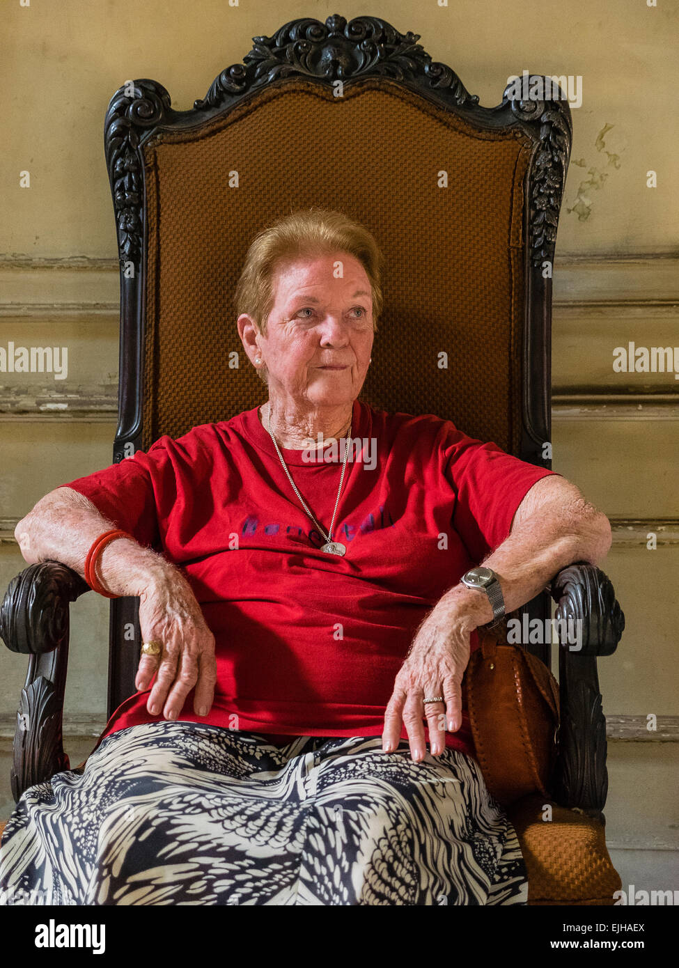The Hispanic Cuban female senior citizen owner and occupant of a pre-revolutionary mansion in the Vedado area of Havana sits in Stock Photo