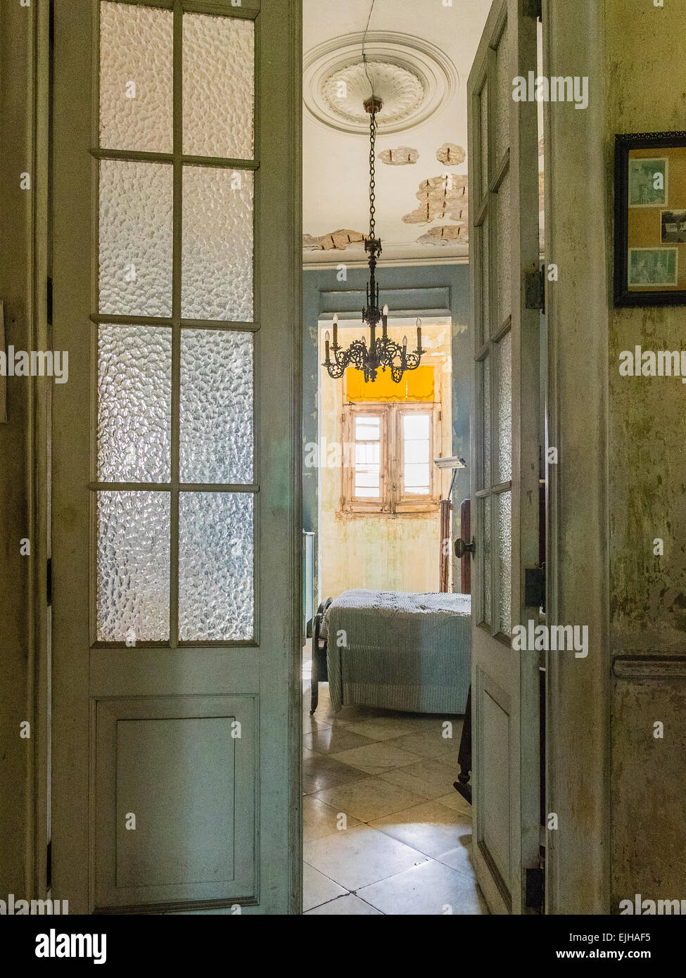 A view through the glass paned doorway to a pre-revolution bedroom with chandelier in an old mansion in Vedado, Cuba. Stock Photo