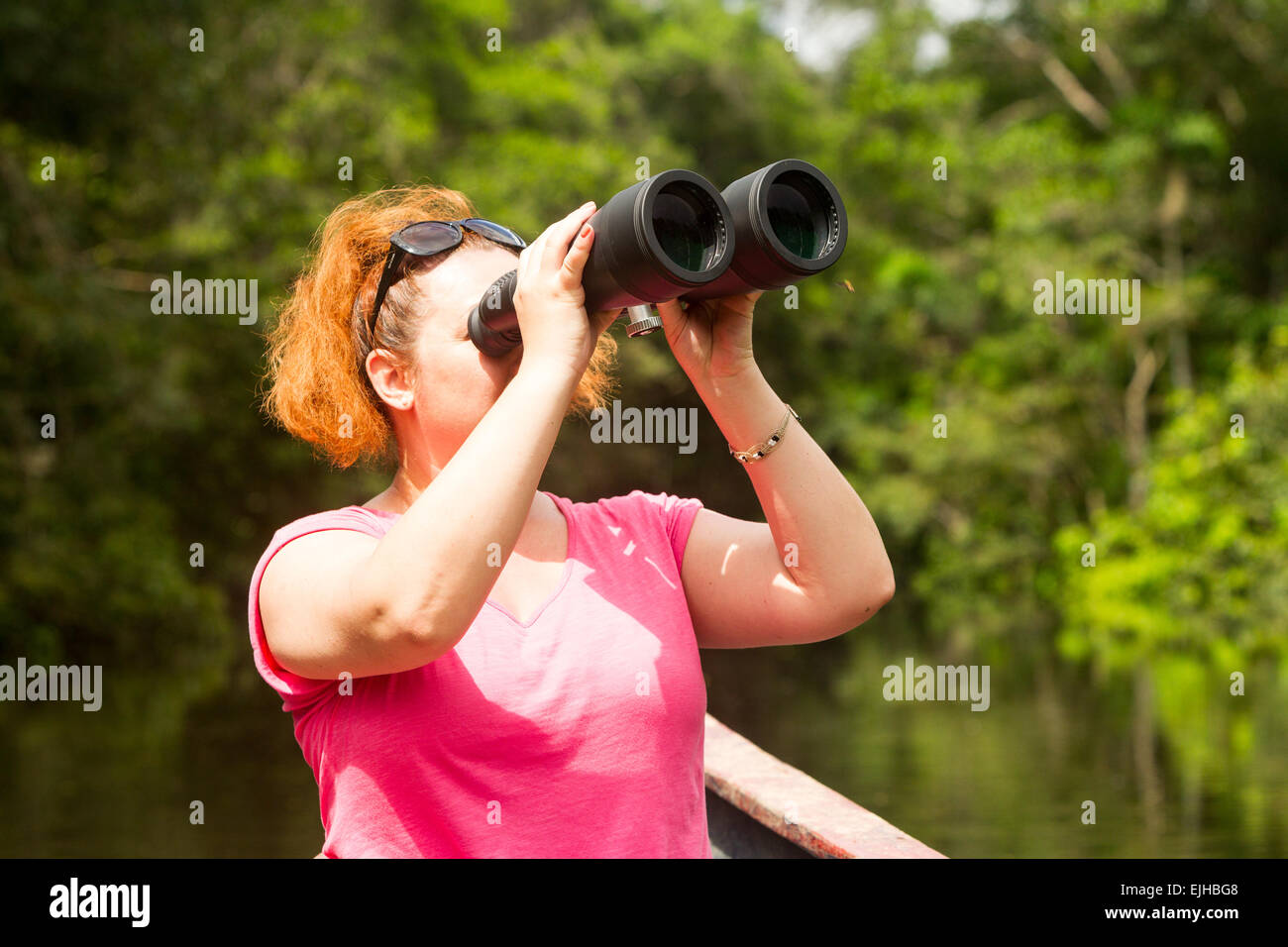 Tourist Woman With High Power Binoculars In Amazon Jungle Against Dense Vegetation Stock Photo