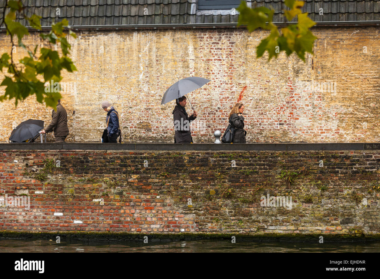 Visitors with umbrellas by canal in Bruges, Belgium Stock Photo