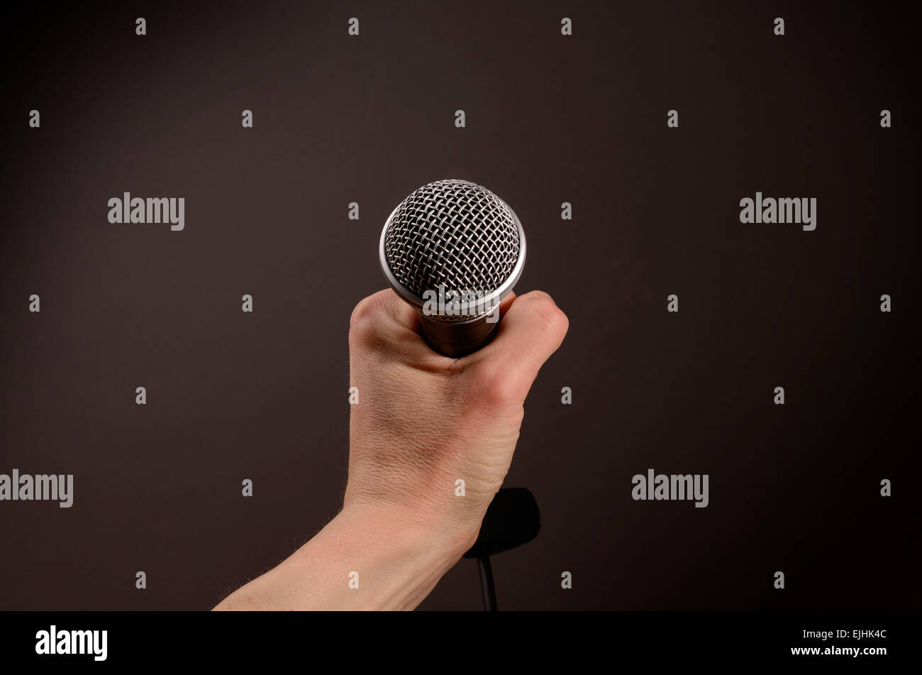 Male hand holding a microphone on a dark background Stock Photo