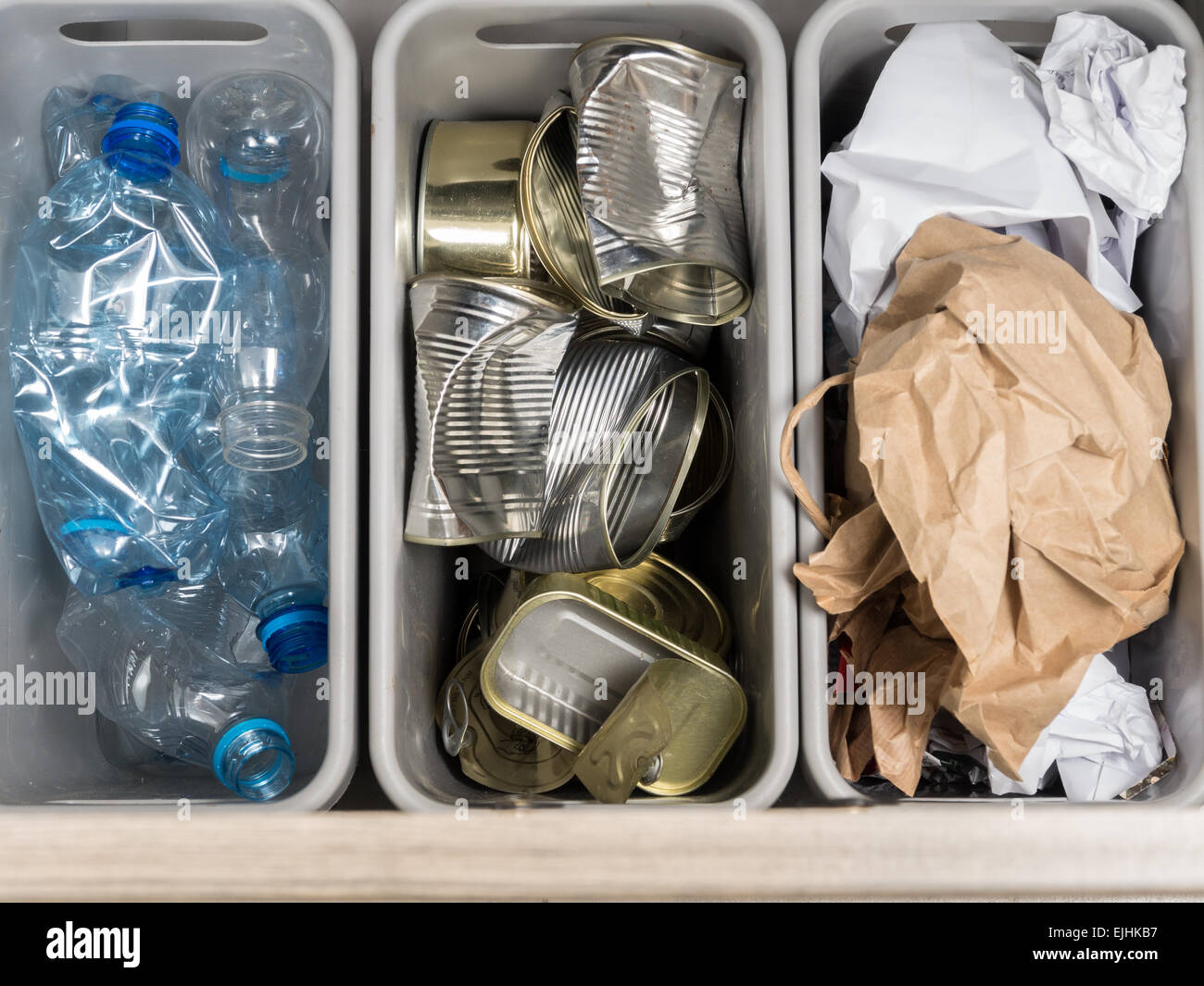 Three plastic trash bins with segregated household garbage - PET bottles, paper and metal cans shot from above Stock Photo