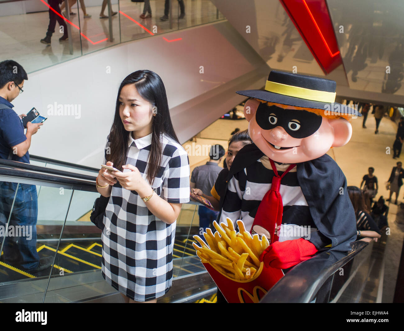 March 27, 2015 - Bangkok, Bangkok, Thailand - A woman rides an escalator ahead of the ''Hamburglar, '' a fast food character used to promote McDonald's restaurants in Thailand, in ''EmQuartier, '' a new mall in Bangkok. ''EmQuartier'' is across Sukhumvit Rd from Emporium. Both malls have the same corporate owner, The Mall Group, which reportedly spent 20Billion Thai Baht (about $600 million US) on the new mall and renovating the existing Emporium. EmQuartier and Emporium have about 450,000 square meters of retail, several hotels, numerous restaurants, movie theaters and the largest man made wa Stock Photo