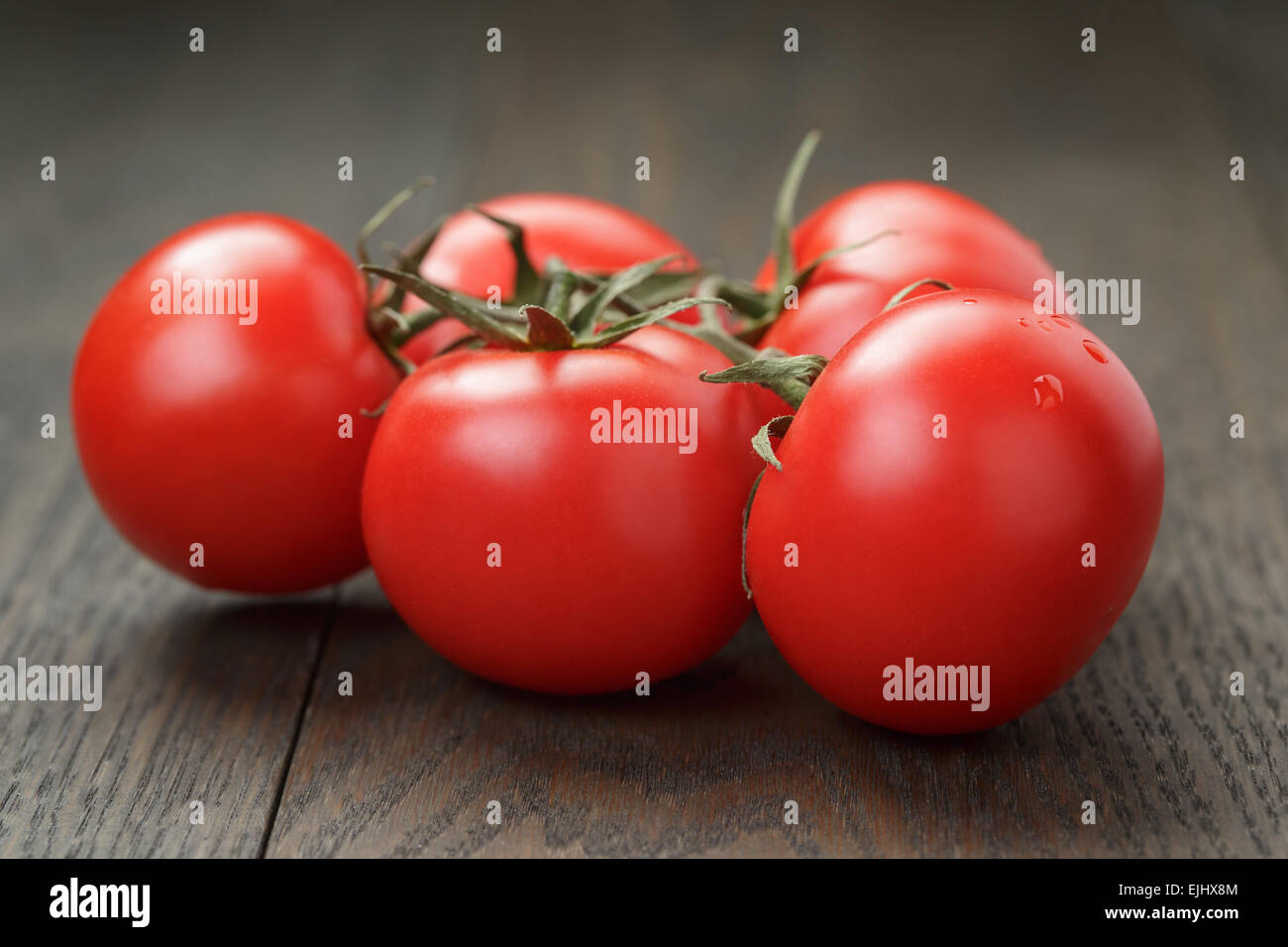 ripe wet tomatoes on vine on wood table Stock Photo - Alamy
