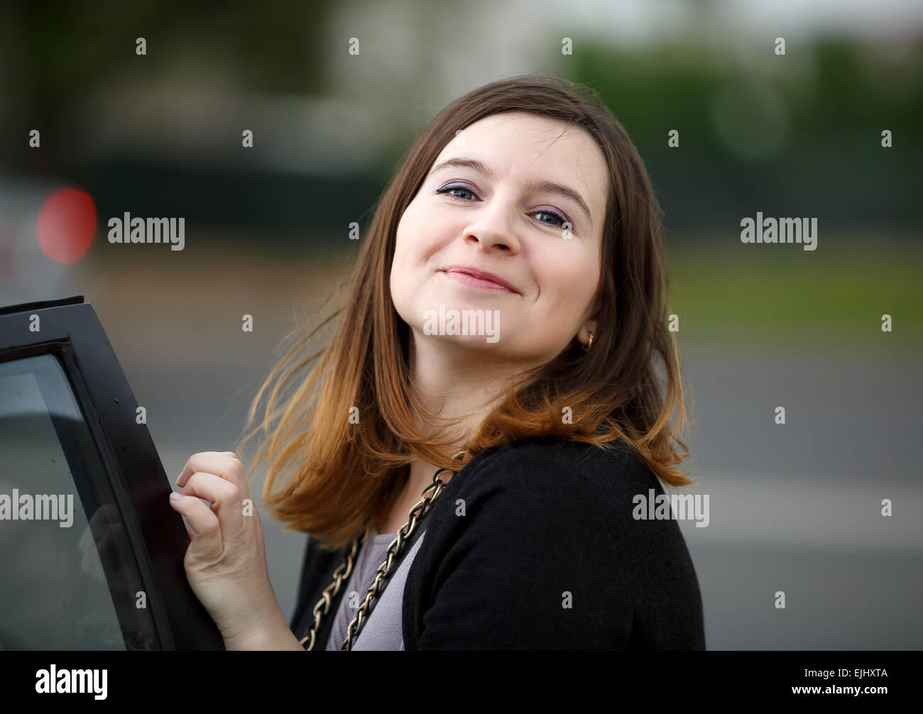 Young woman with long hair posing in the street, looking at the camera and smiling. Shallow depth of field. Focus on the model's Stock Photo