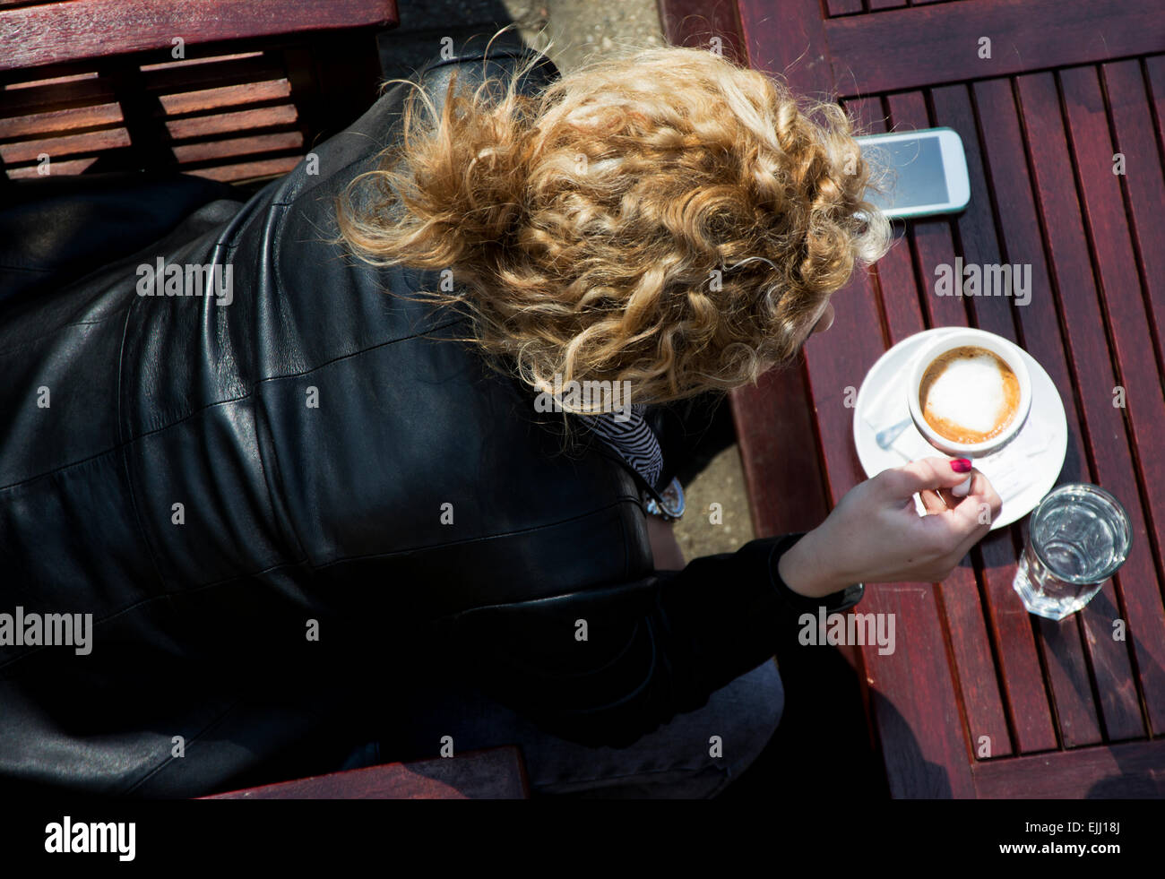 Pretty young woman with blond curly hair sitting  on a coffee break.Shot from a above.She is drinking coffee and communicating w Stock Photo