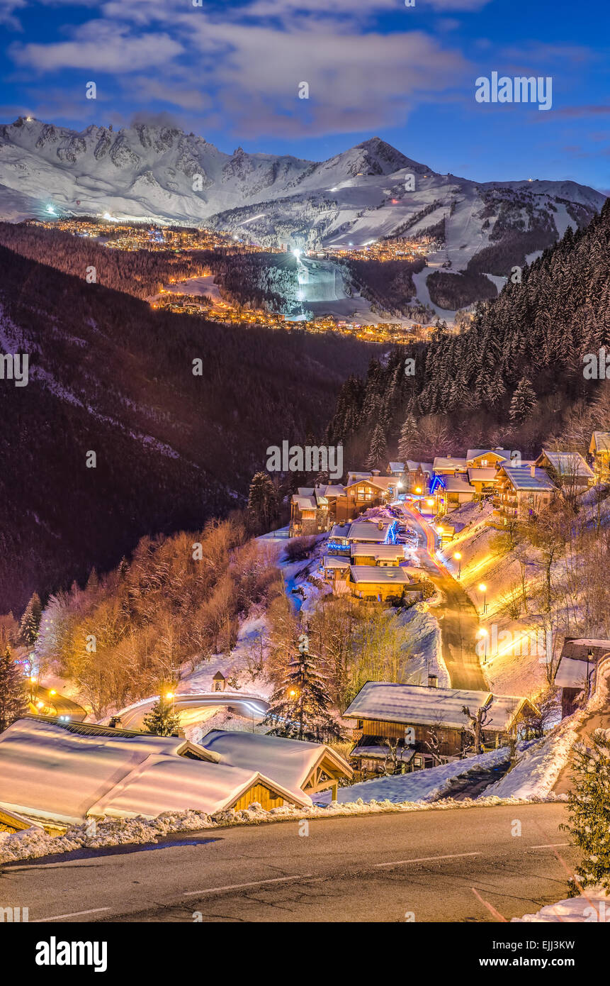 Small village on snowy mountain, winter, blue hour, light trails, ski slope, mountain top in the distance under blue cloudy sky Stock Photo