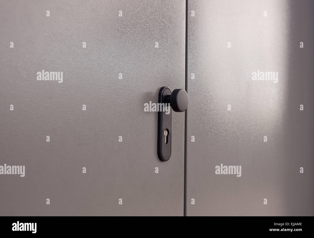 Black doorknob over isolated grey background of the door, outdoors side Stock Photo
