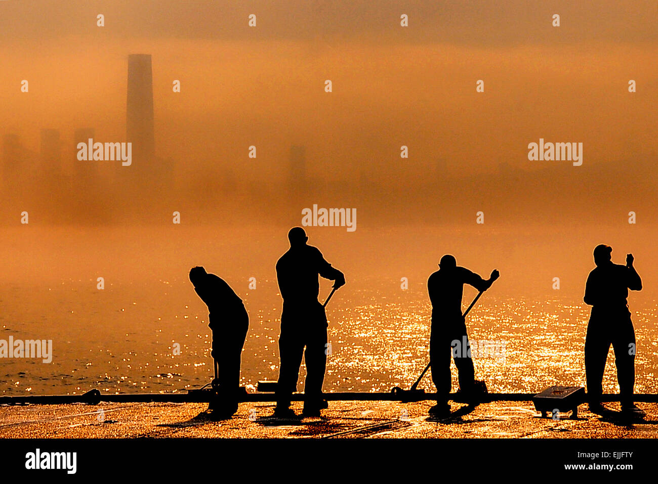 A US Navy sailors scrub the flight deck of the command ship USS Blue Ridge on a hazy evening in Victoria Harbor March 20, 2015 in Hong Kong. Stock Photo