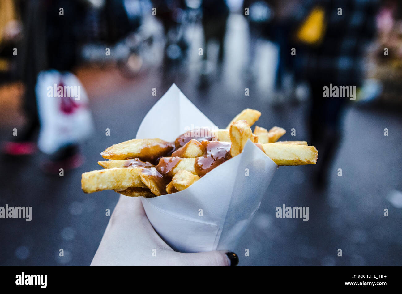 Hand holding a cone of Frites in satay sauce in Amsterdam Netherlands