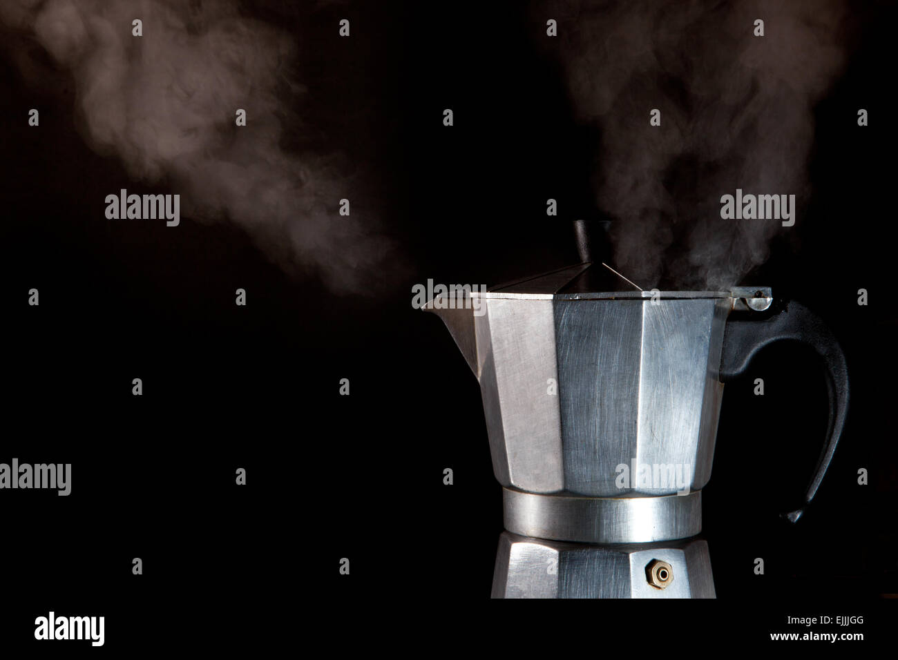 Steaming espresso coffee maker at work isolated over black background