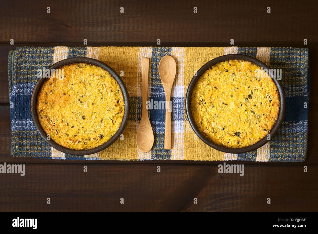 Overhead shot of traditional Chilean corn pie called Pastel de Choclo served in bowls, photographed on cloth on dark wood Stock Photo