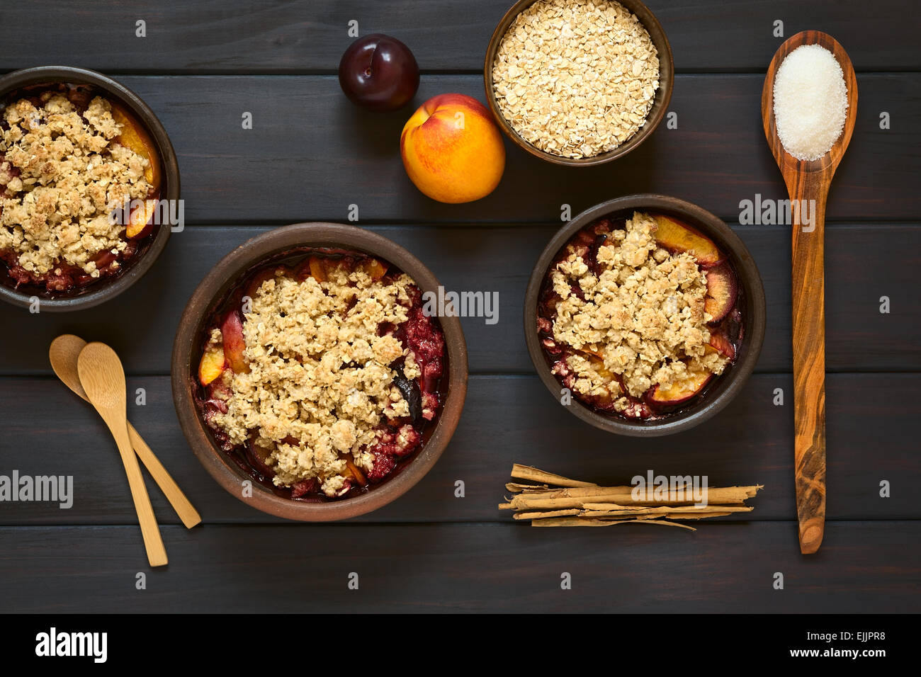 Overhead shot of rustic bowls filled with baked plum and nectarine crumble or crisp, photographed on dark wood Stock Photo