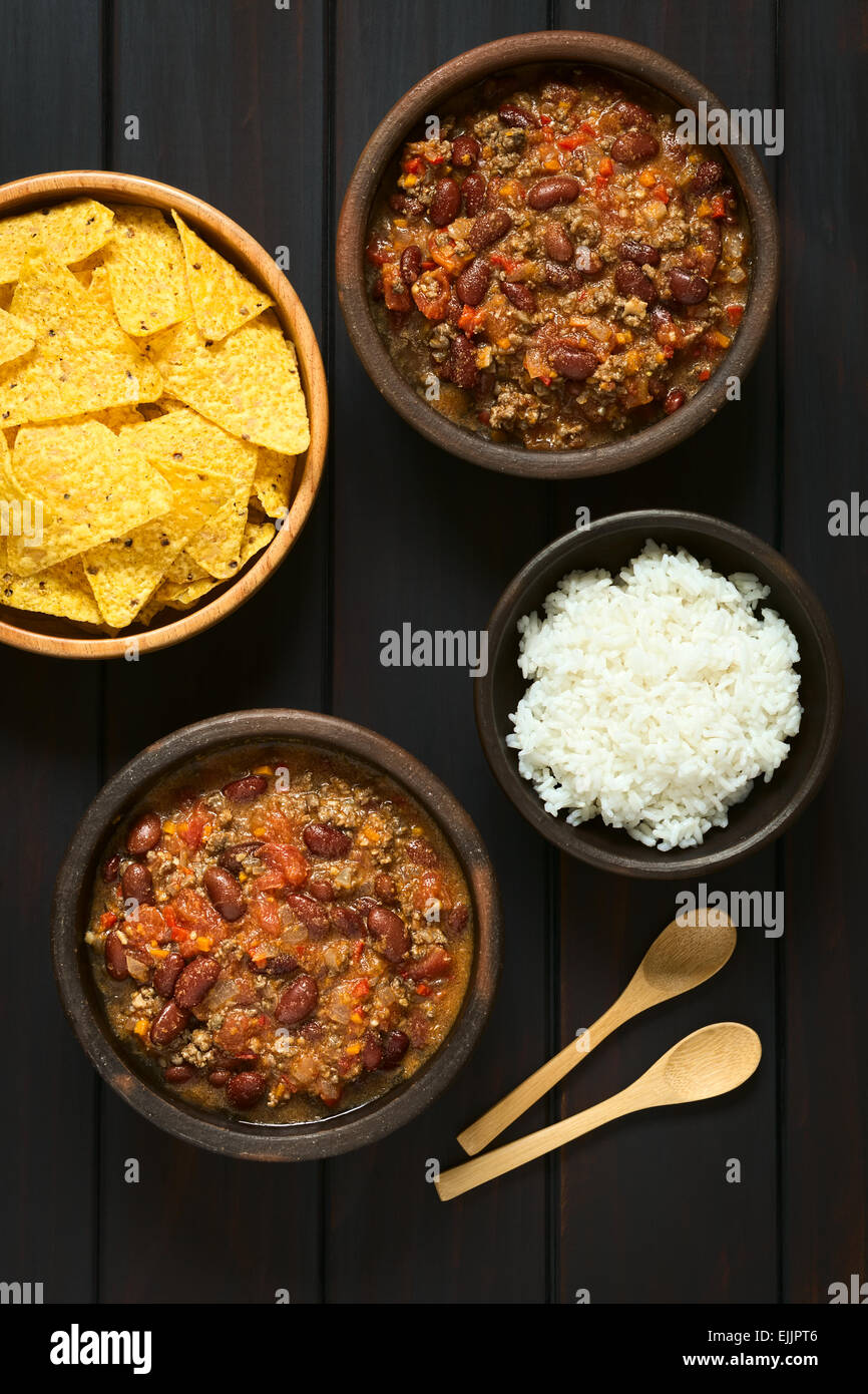 Overhead shot of two bowls of chili con carne with rice and tortilla chips, photographed on dark wood with natural light Stock Photo