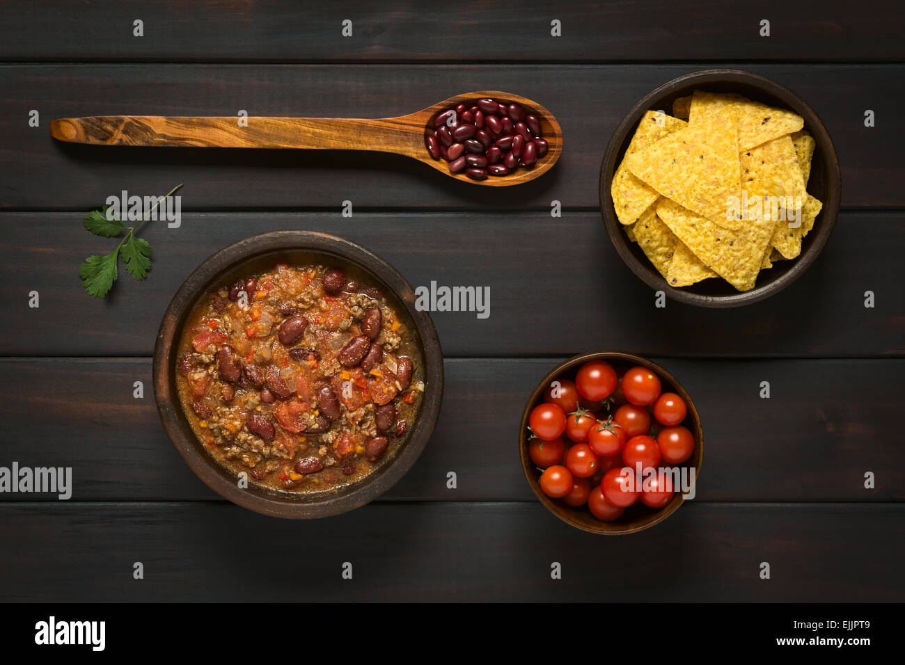 Overhead shot of chili con carne and tortilla chips with ingredients dried kidney beans and cherry tomatoes Stock Photo