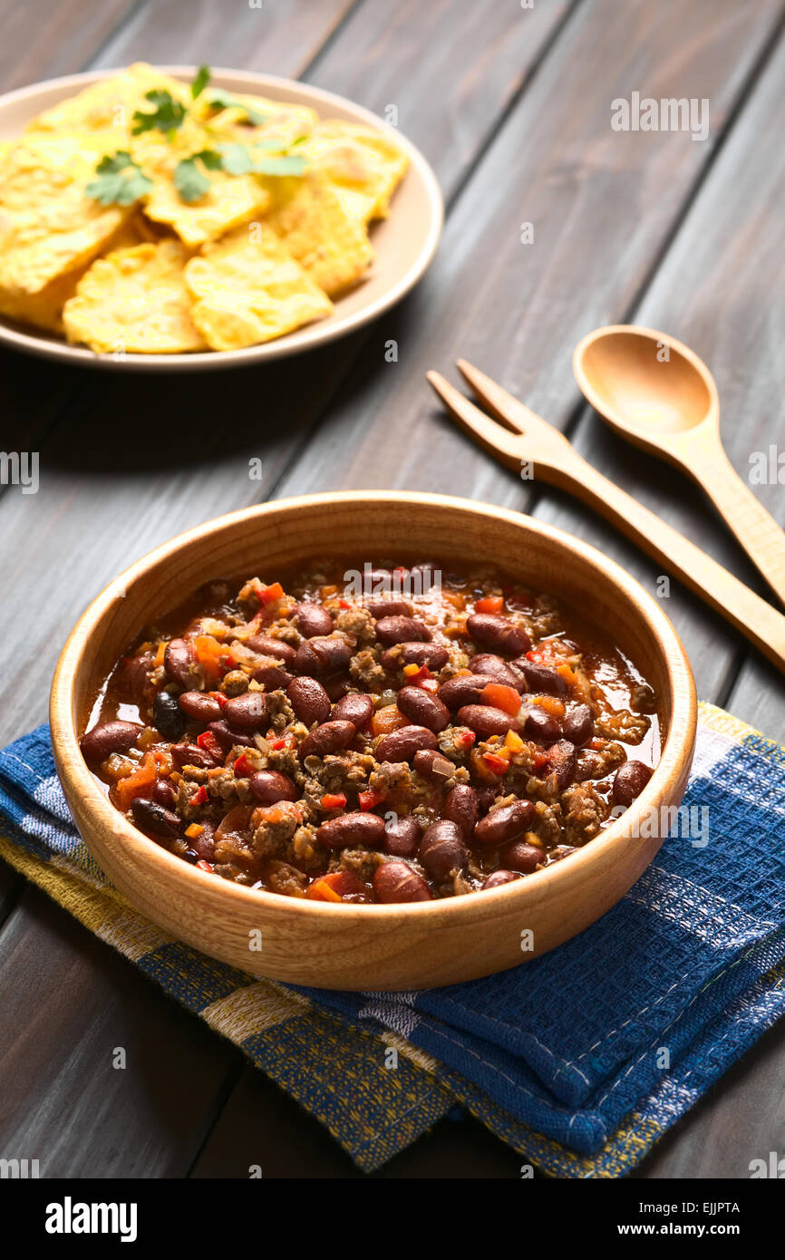 Wooden bowl of chili con carne with homemade tortilla chips in the back, photographed with natural light (Selective Focus) Stock Photo