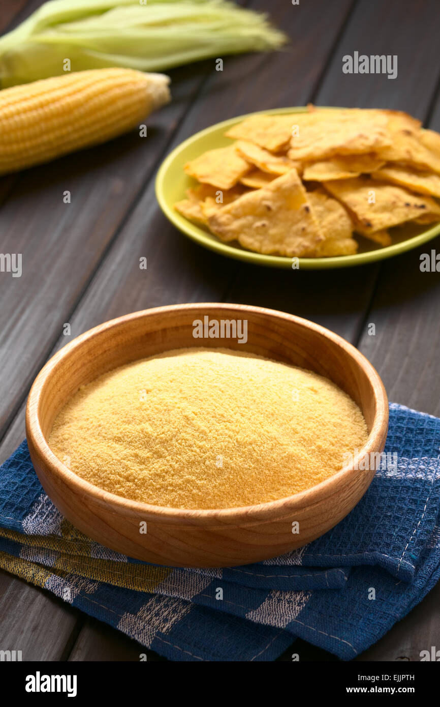 Wooden bowl of cornmeal with homemade tortilla chips and cobs of corn in the back, photographed