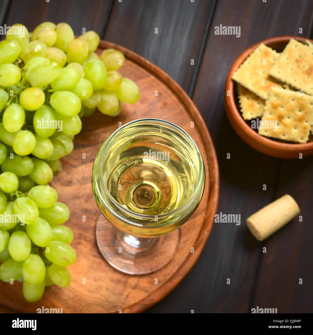 Glass of white wine with white grapes, crackers and a cork