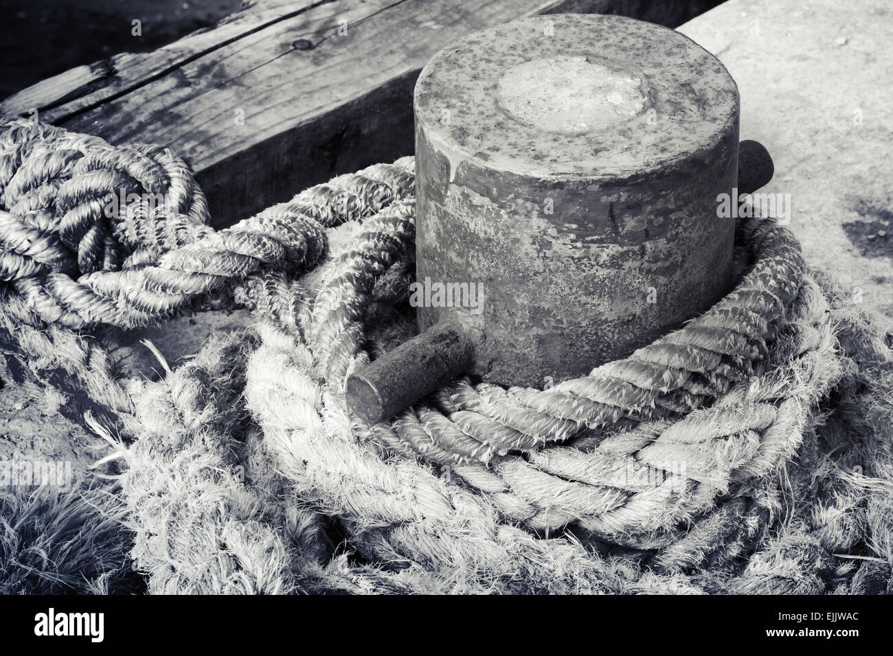 Old rusted mooring bollard with naval ropes on the pier, black and white photo Stock Photo