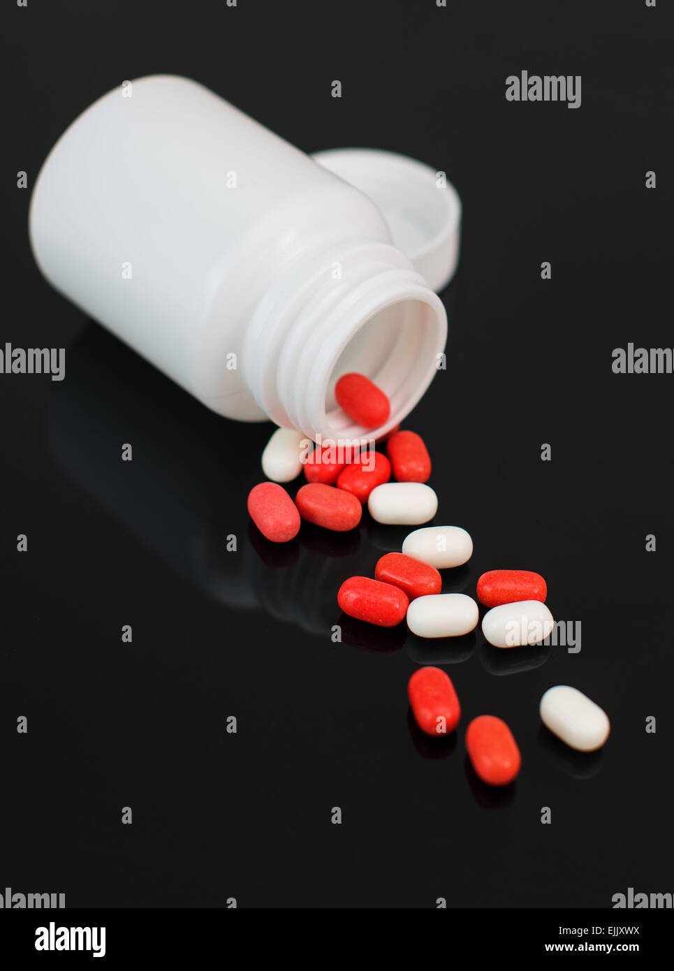 Red and white pills spilled from bottle. Stock Photo