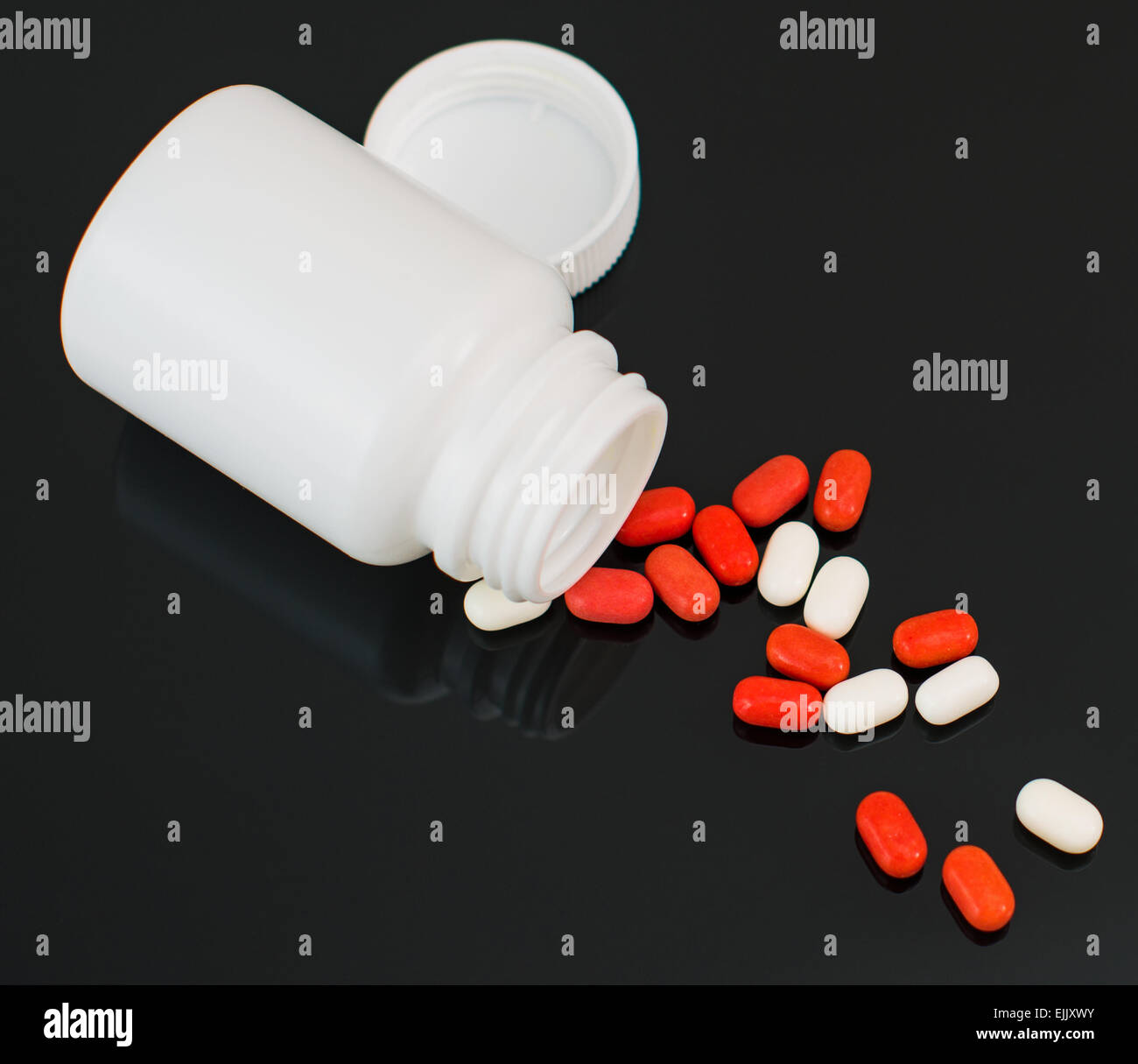 Red and white pills spilled from bottle. Stock Photo