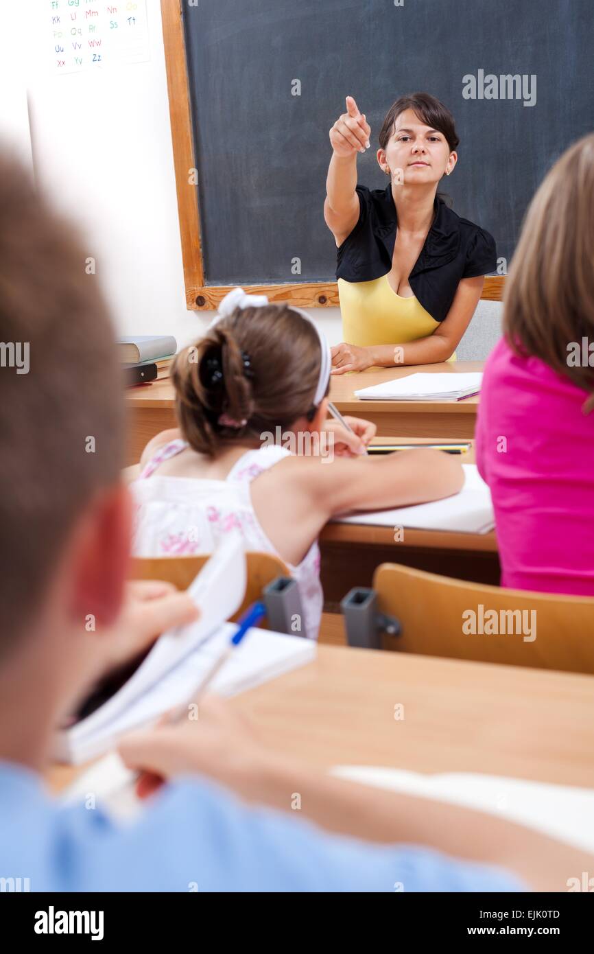 Teacher making sign with hand to a cheating student who looks into book while writing test Stock Photo
