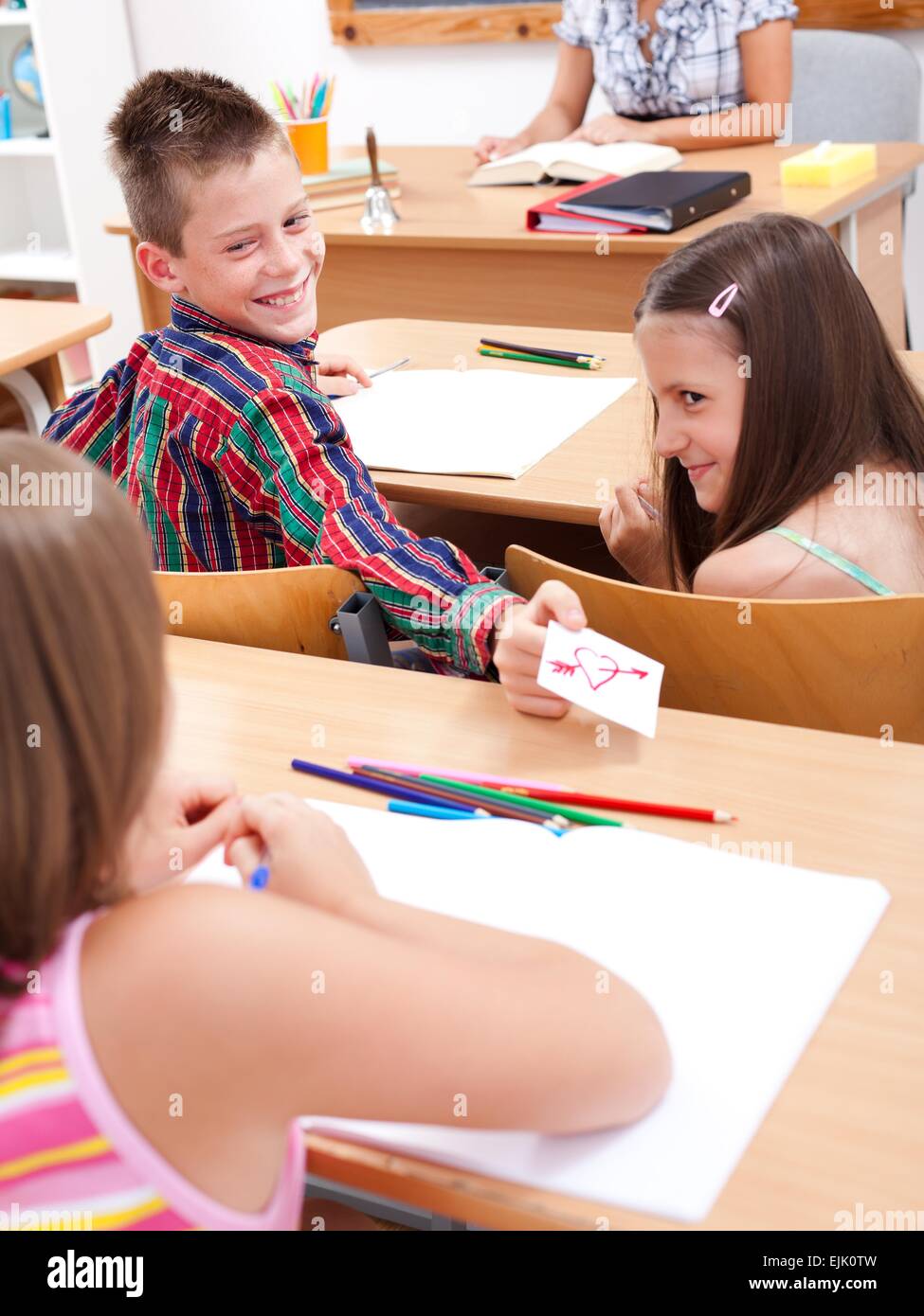 Cheerful elementary school boy giving love letter to his classmate during class Stock Photo