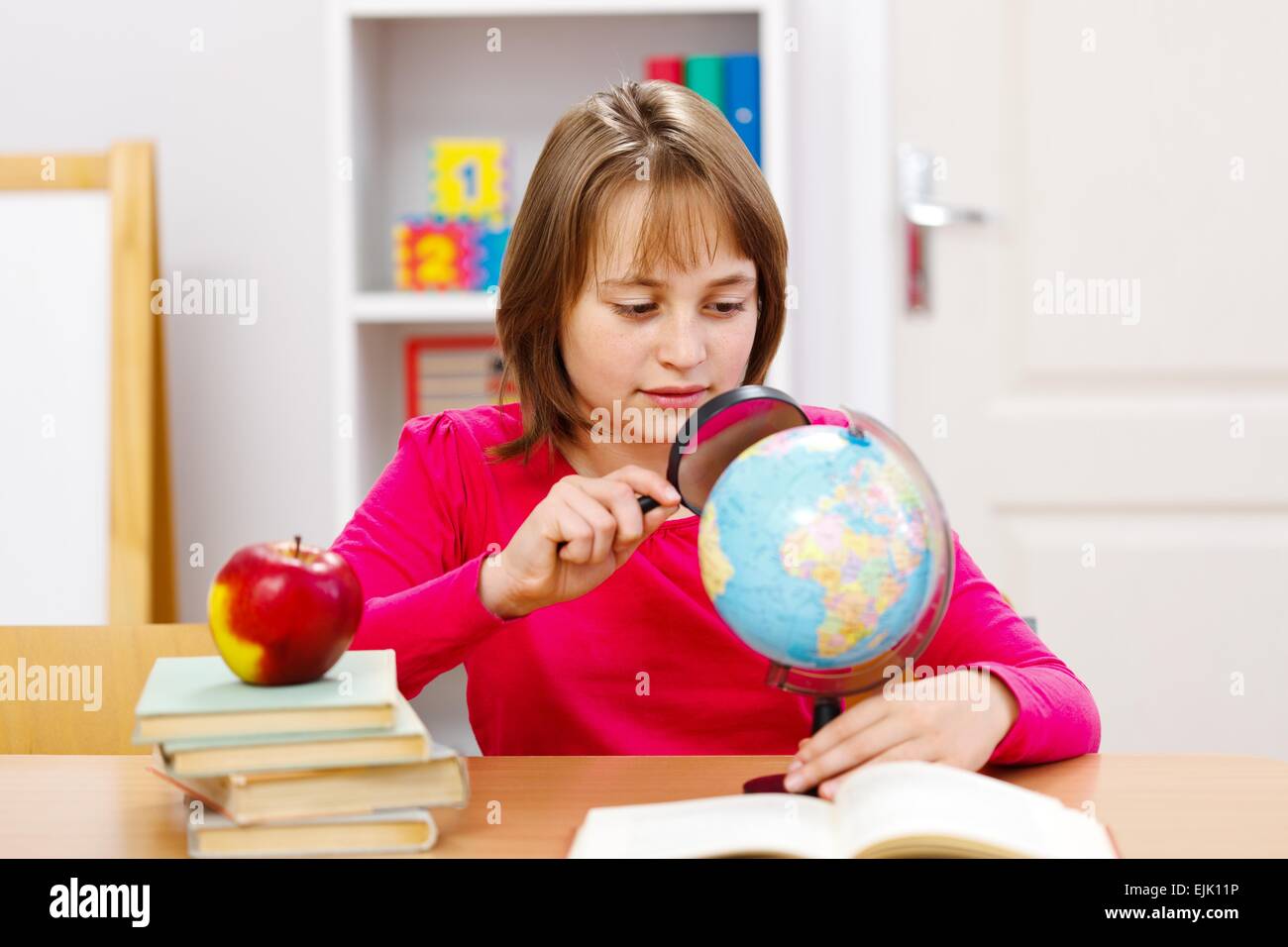 Schoolgirl on geography class, looking at Earth globe with magnifier Stock Photo