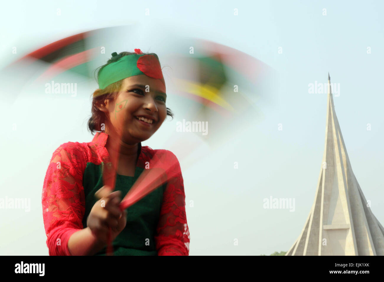 A Bangladeshi child holds a national flag as she stands in front the National Monument for the Martyrs of the Liberation War of Bangladesh in Savar Stock Photo