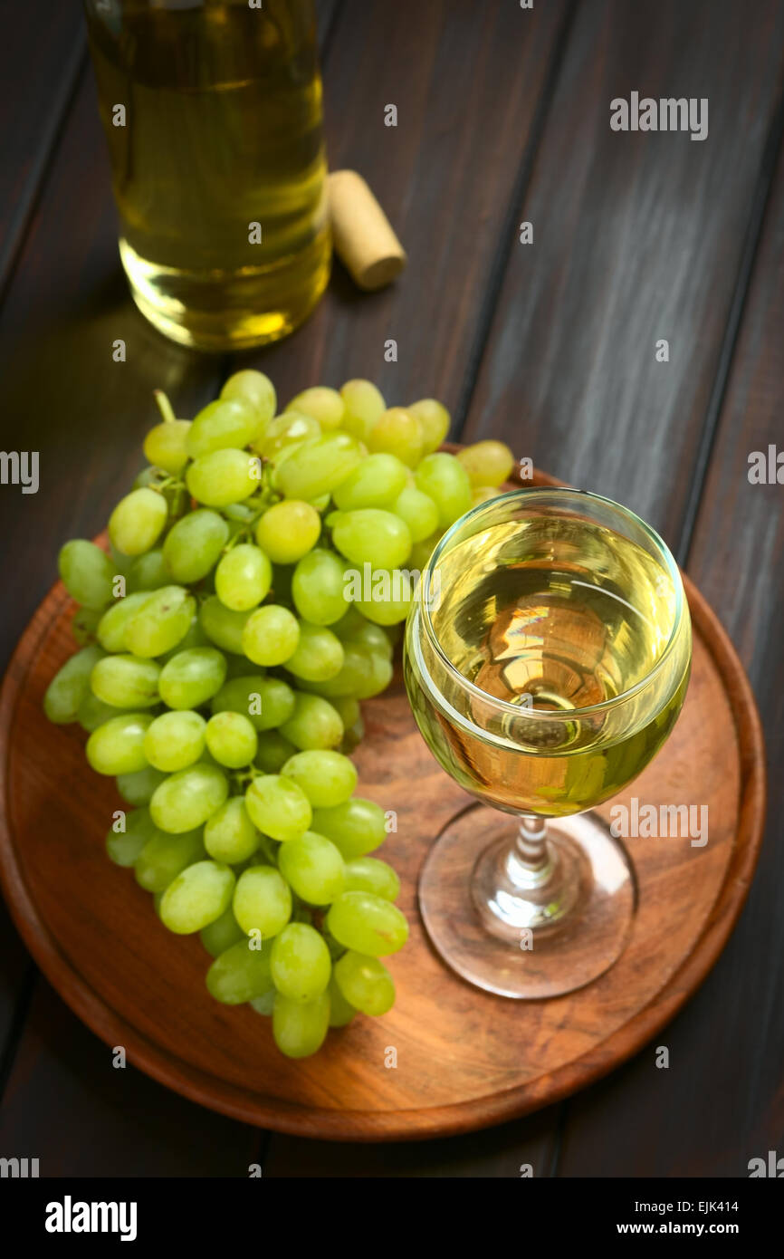 Glass of white wine with white grapes and a bottle of wine