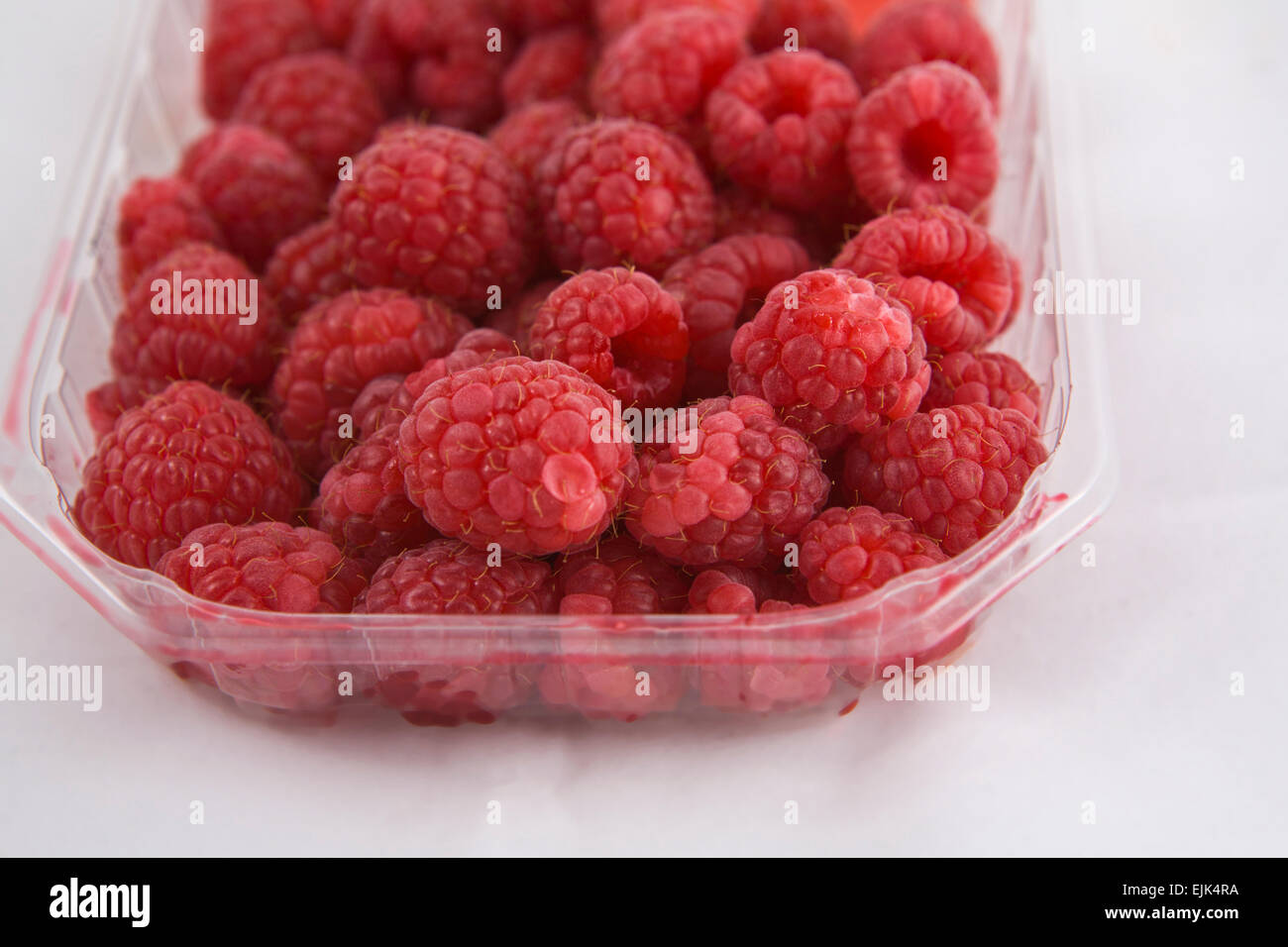 Plastic box of fresh raspberries, isolated over white background Stock Photo