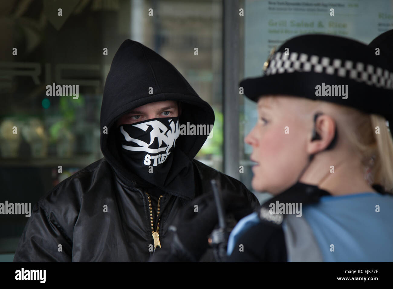 Masked demonstrator at the National Front neo-nazi rally & White Pride Demo in Piccadilly Manchester confronts a policewoman.  Arrests  made as Far Right 'White Pride' group gathered in Manchester to stage a demonstration. Around 50 members of the group waved flags and marched through Piccadilly Gardens.  Anti-fascist campaigners staged a counter-demonstration with police separating the two sides.  Greater Manchester Police said two arrests were made, one for a breach of the peace. The second was also held over a public order offence. Stock Photo