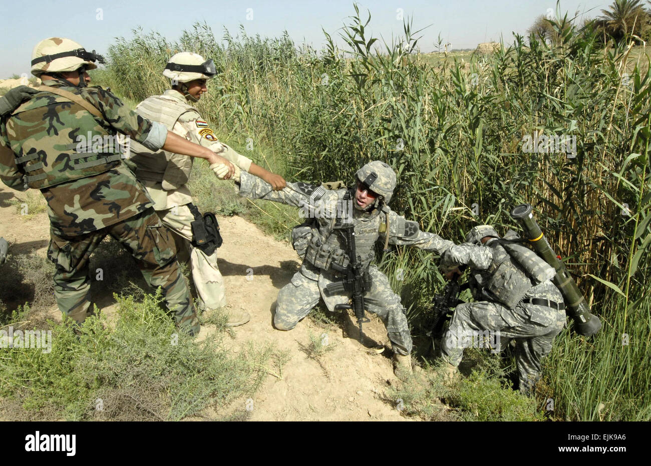 U.S. Army Sgt. Steven Calhoun is assisted by Iraqi army soldiers in pulling out a Soldier after he fell into an irrigation ditch during a joint mission in Khan Bani Sa'ad, Iraq, July 12, 2007.  Soldiers from Alpha Battery, 2nd Battalion, 12th Field Artillery Regiment, 4th Stryker Brigade Combat Team, 2nd Infantry Division and units of the Iraqi army are conducting a cordon and search mission to clear the area of insurgents and cache sites.  Mass Communication Specialist 2nd Class Scott Taylor Stock Photo