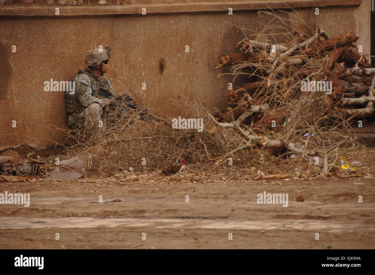 A U.S. Army Soldier from Baker Company, 1st Battalion, 15th Infantry Regiment, 3rd Heavy Brigade Combat Team, 3rd Infantry Division uses a pile of dead branches for cover as he scans for enemy personnel during a patrol through a village southeast of Salman Pak, Iraq, Feb. 15, 2008. The Soldiers are working with sheiks in the area to improve security after Al-Qaeda members had recently occupied the are.  Sgt. Timothy Kingston Released Stock Photo