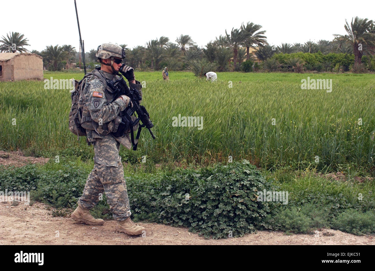 An Iraqi family works in a field as U.S. Army Sgt. Sean Reed, a team leader with 1st Squadron, 40th Cavalry Regiment, 4th Brigade Combat Team Airborne, 25th Infantry Division, strolls past during a reconnaissance patrol in Adwaniya, Iraq, April 7, 2007.  The 1/40th CAV is responsible for the security of the area surrounding the South Baghdad suburb.  Staff Sgt. Sean A. Foley Stock Photo