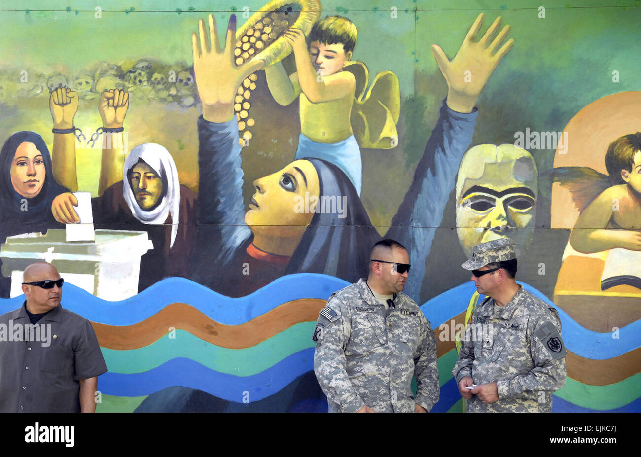 Two U.S. Army Soldiers and a personal security officer stand in front of a mural from a local artist depicting scenes of freedom and the historic Iraqi elections in Baghdad, Iraq, June 16, 2007.  Cherie A. Thurlby. Stock Photo