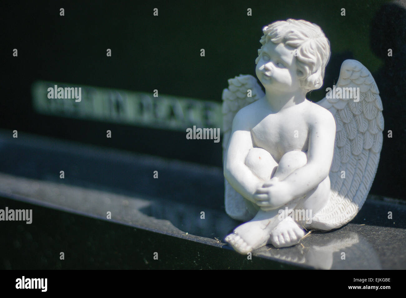 Small angel sitting on plinth of black granite gravestone with inscription 'rest in peace' Stock Photo