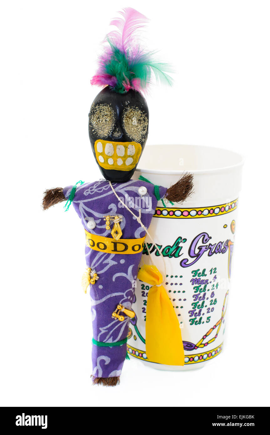 Voodoo doll with charms, pins and hair bag beside a plastic cup listing dates of the Mardi Gras in New Orleans Stock Photo
