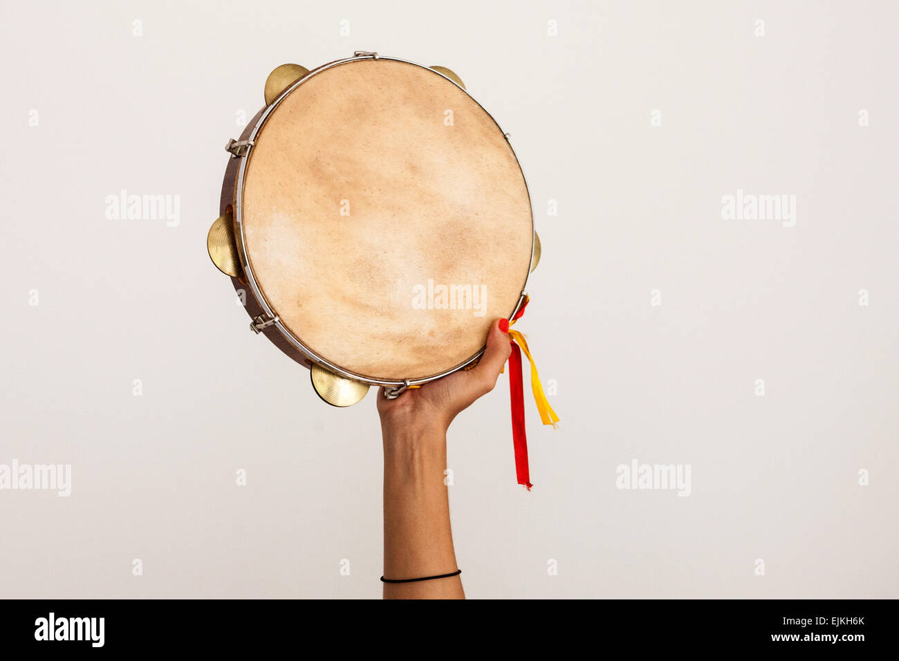 Hand holding tambourine with yellow and red ribbons on white background Stock Photo