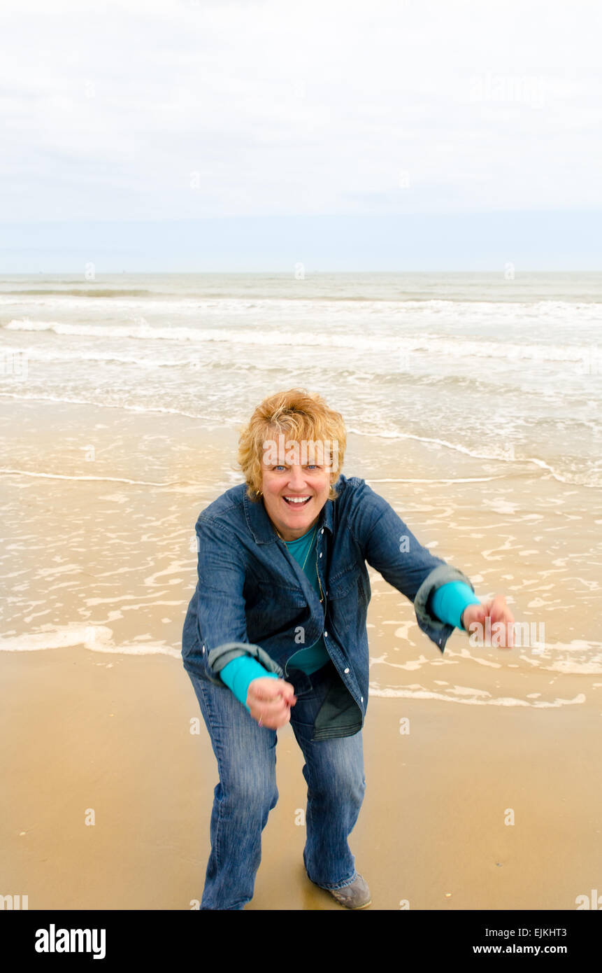 Senior woman on the beach having fun and about to jump for joy Stock Photo