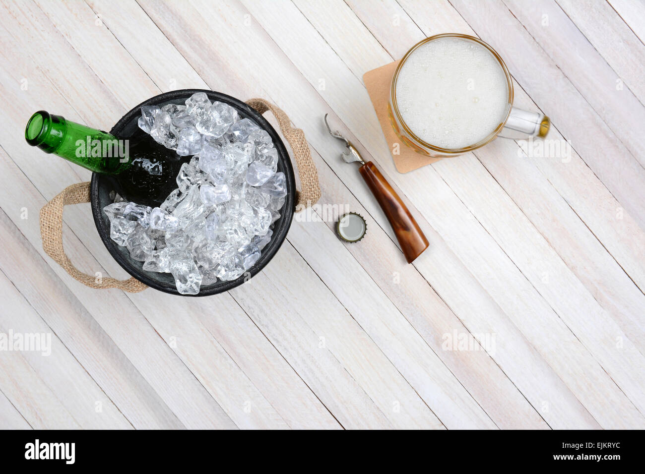 Overhead shot of an ice bucket with an opened beer bottle, a mug of beer and opener on a rustic white wood table. Horizontal for Stock Photo