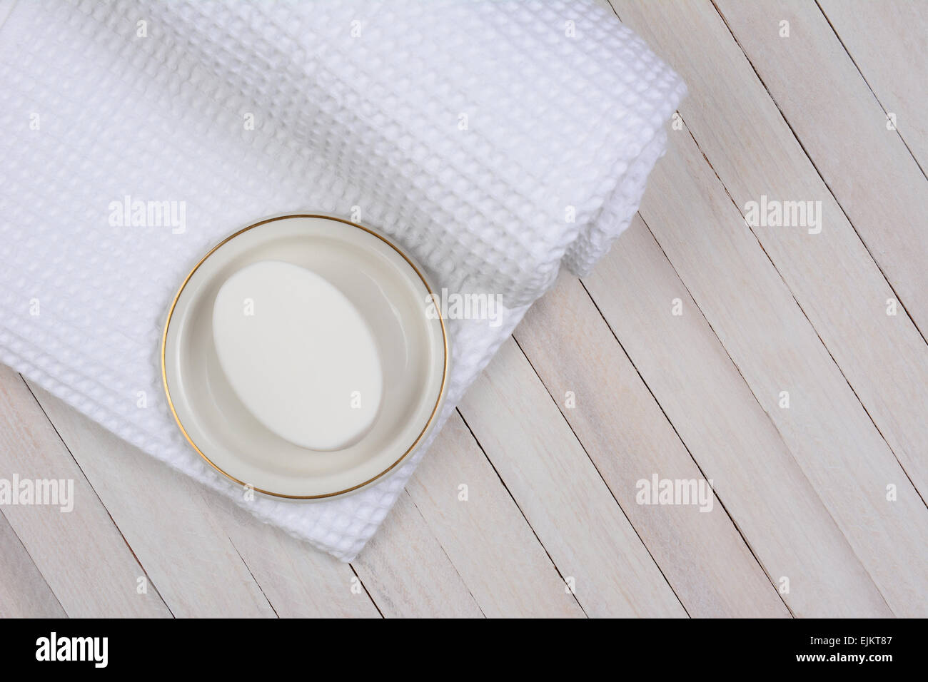 High angle shot of a white bath towel on a whitewashed wood surface. On the towel is a bar of soap in a dish. Stock Photo
