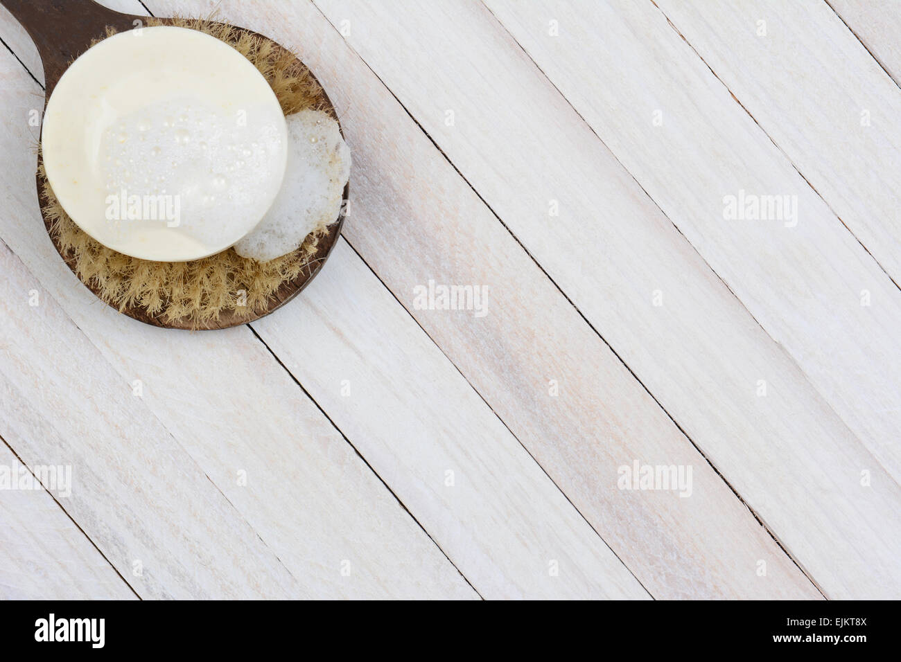 High angle shot of a sudsy bar of soap on a scrub brush. On a rustic wood surface the brush and soap are in the upper left corne Stock Photo