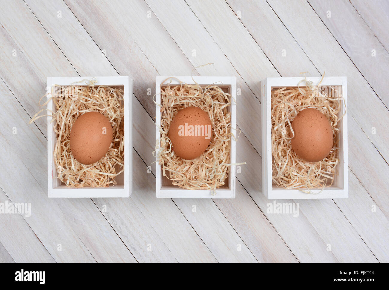 Three brown eggs in wood crates on a whitewashed wood surface. High angle shot in horizontal format. Stock Photo