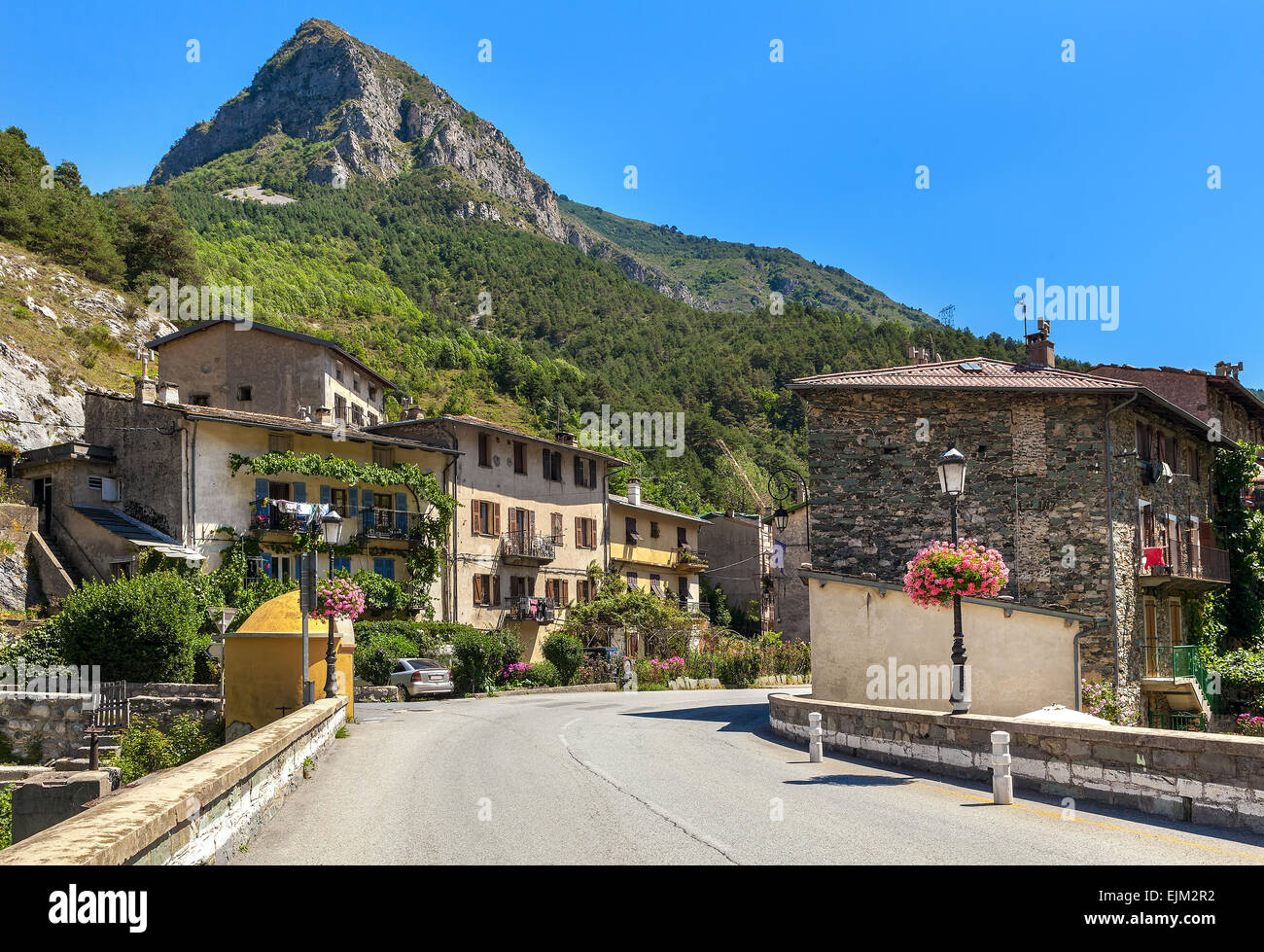 Road, rural houses and mountain on background under blue sky in small town of Tende, France. Stock Photo