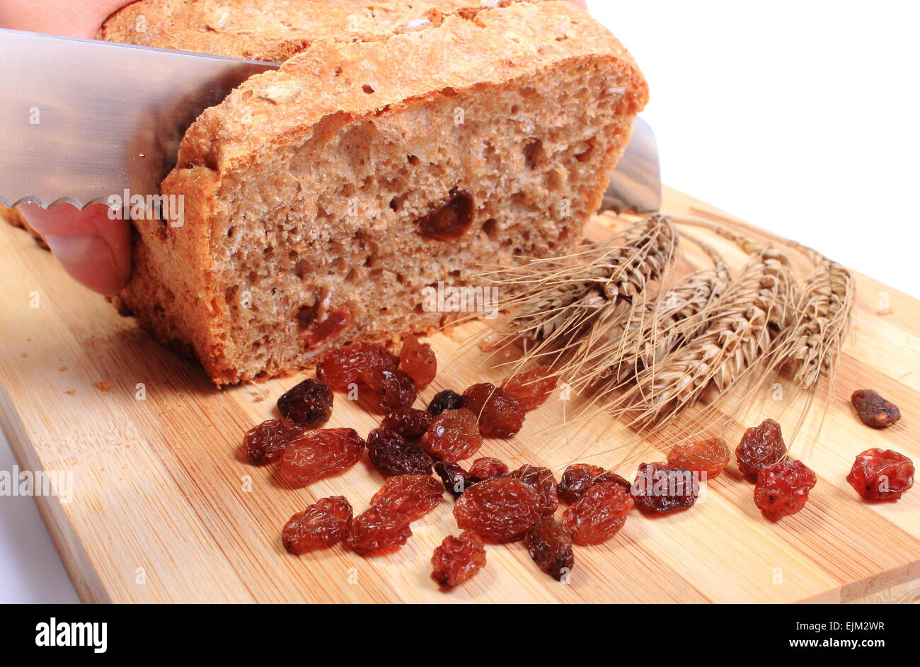 Slicing fresh baked wholemeal bread, ears of wheat and heap of raisins ...