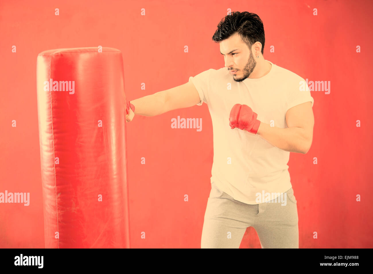 young boxer in training on a punching bag in a gymnasium warm filter applied Stock Photo