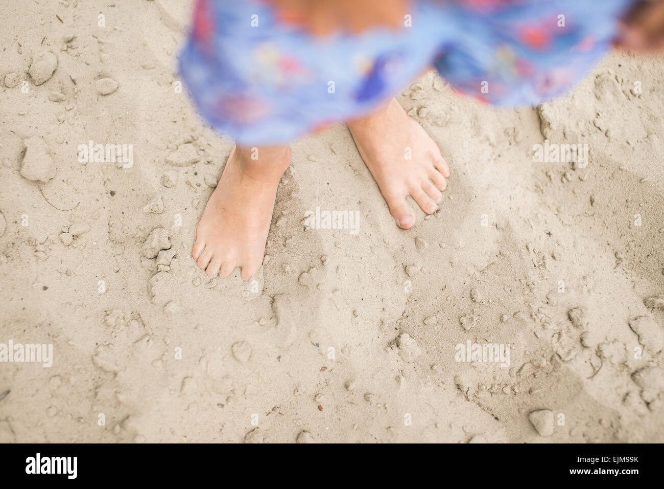 Toddler feet on sand at the beach. Child in blue shorts walking barefoot. Having fun at summertime. Stock Photo