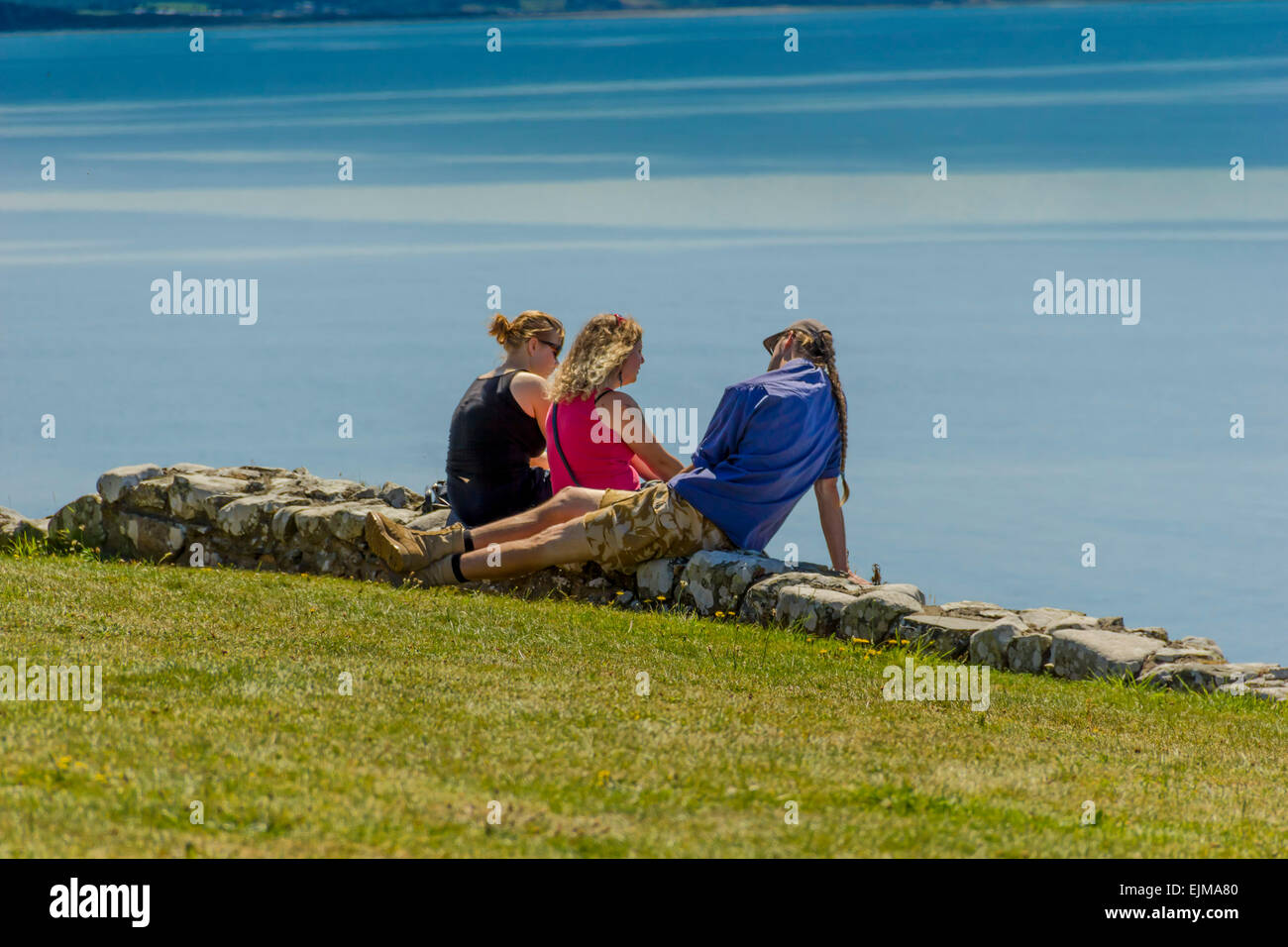 Three young people sunbathing at Criccieth Castle, North Wales, Gwynedd, United Kingdom. Stock Photo